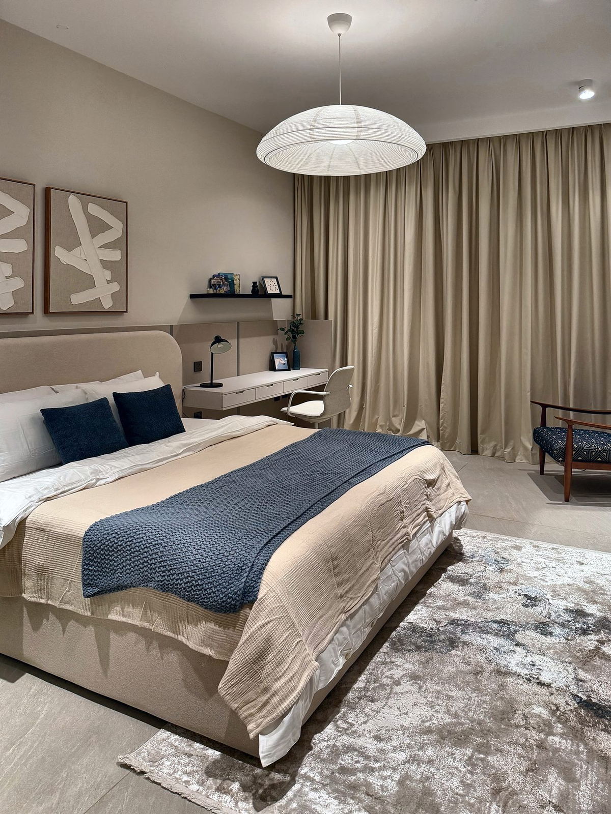 Bedroom at night lit by a large paper pendant, with a knitted blue throw