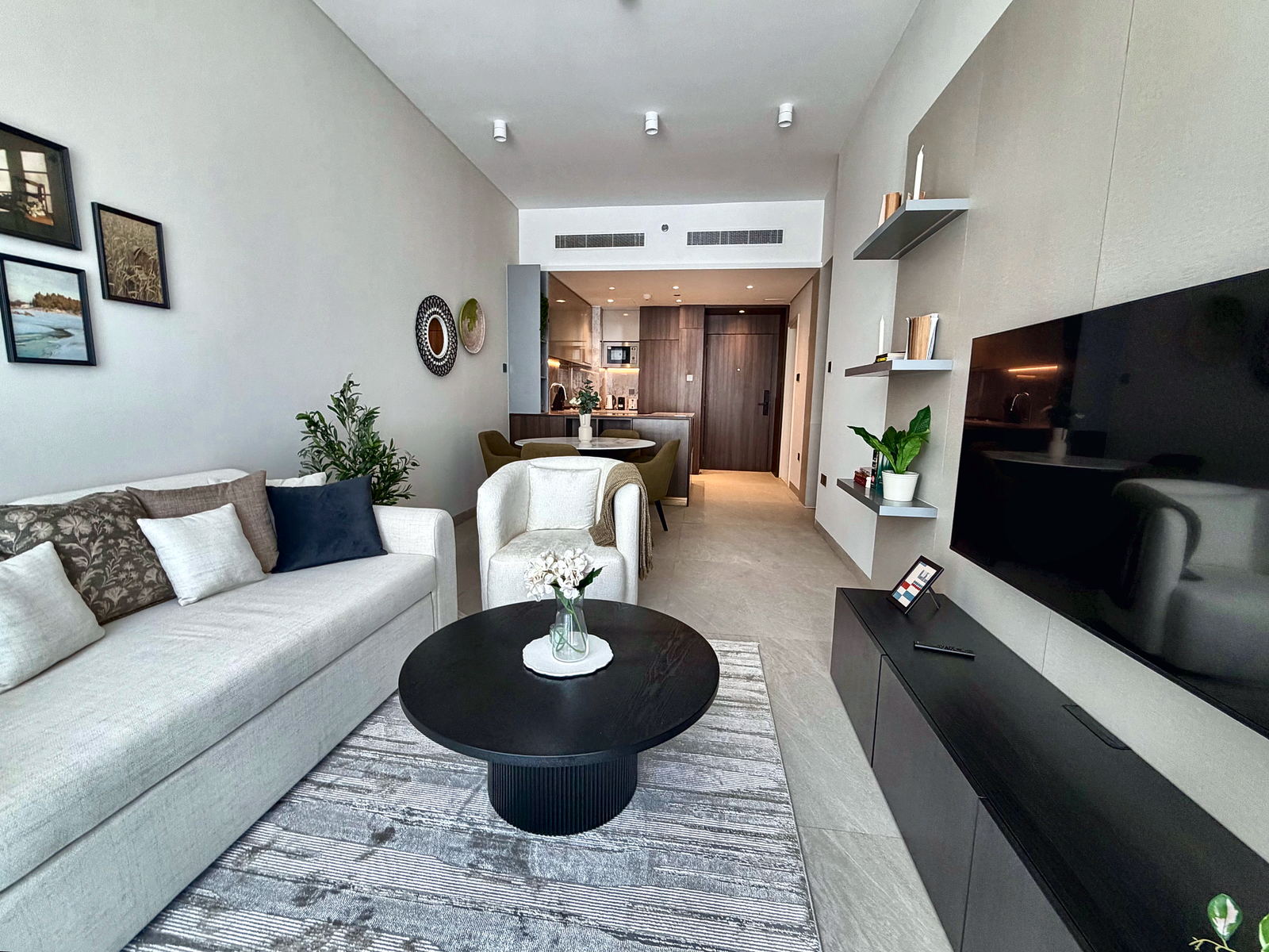 Open-plan living room with linen sofa, black round coffee table, and dining nook by the kitchen
